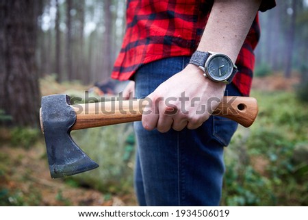 Lumberjack bush crafter holding an axe in the woods in checked shirt.