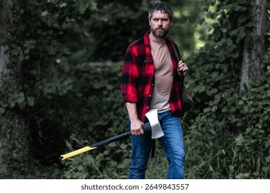 Lumberjack cutting the tree by the axe. Handsome man with an ax in the forest. Handsome man or lumberjack, bearded hipster in checkered shirt with axe. A bearded lumberjack with a large ax.