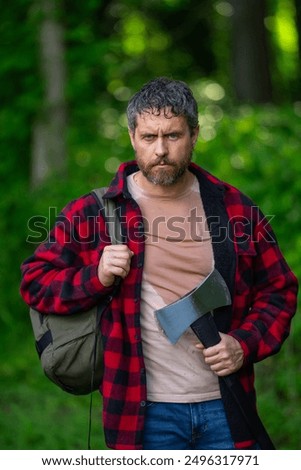 Lumberjack in forest. Photo of the lumberjack in the woods. Strong woodcutter. Portrait of mature lumberjack with axe outdoor. Man hold rusty axe. Double blade axe. Lumberjack with ax chopping wood