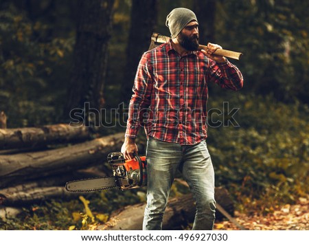 Lumberjack worker standing  in the forest with axe and chainsaw
