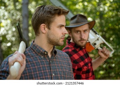 Lumberjack workers in the forest. Woodcutter with axe and lumberjack with chainsaw. Handsome woodcutter men hipsters in forest
