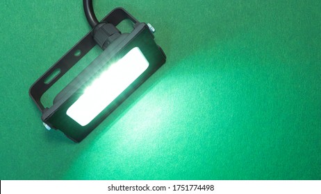 Luminous diode floodlight. Lighting device. Modern energy-saving technologies. Lighted bright green background. Copy space for text.