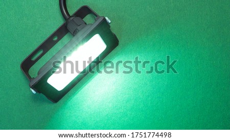 Luminous diode floodlight. Lighting device. Modern energy-saving technologies. Lighted bright green background. Copy space for text.