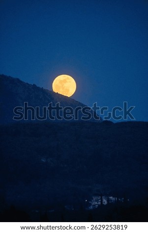 A luminous full moon ascends, casting an ethereal glow upon a mountainous horizon in the twilight.