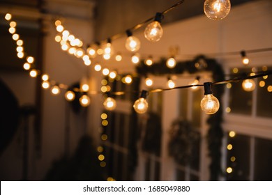 Luminous incandescent lamps hang in the form of a garland on wires, against the background of a shop window. Background from a garland. Incandescent lamps. - Powered by Shutterstock