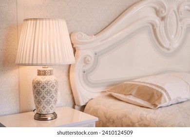 Luminous lamp with a lampshade stands near the bed on the bedside table