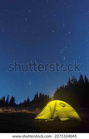 Luminous tourist tent under the starry sky. Tourist tent at night in the forest. Starry sky above the tent. Vertical frame.