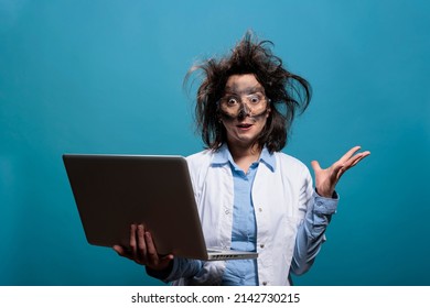 Lunatic chemist with messy hair and dirty face having laptop while gesticulating angrily after dangerous lab explosion. Insane scientist being enraged after failed laboratory chemical experiment.