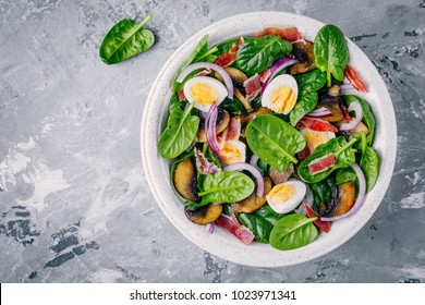 Lunch Bowl Of Spinach Salad With Bacon, Mushrooms, Eggs And Red Onions On Gray Background