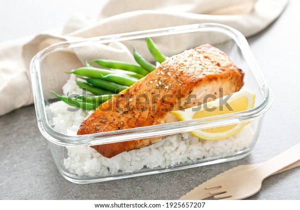 Lunch box container with grilled salmon fish\
fillet, rice and green\
beans
