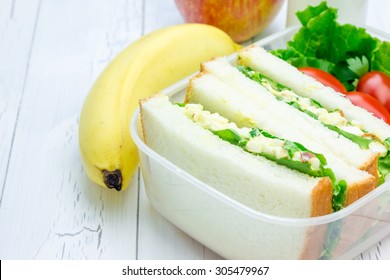 Lunch box with egg salad sandwiches, apple, banana and milk