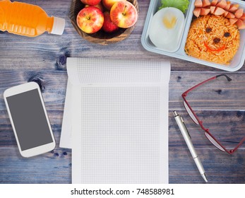 Lunch Box For Kids With Mobile Phone And Note Pad On Wooden Background. Back To School Concept.