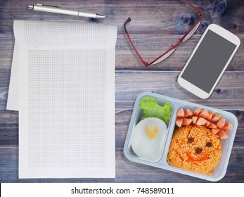 Lunch Box For Kids With Mobile Phone And Note Pad On Wooden Background. Back To School Concept.