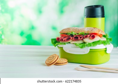 Lunch Box With Sandwich Near Biscuits In Front Of Thermos Mug On White Wooden Background With Copy Space; Selective Focus