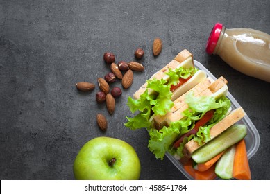 Lunch Box With Sandwich, Vegetables, Juice, Nuts And Apple On Black Background. Healthy Eating. Flat Lay.