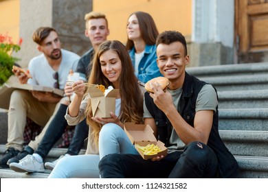 Lunch Break With Friends. Group Photo Of Students Sitting On Stairs And Eating Takeout Food: Pizza, Asian Noodles, Potato Frites And Burger.