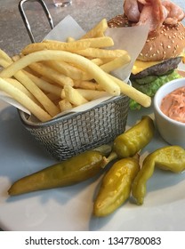 Lunch In A Cafe. French Fries In A Metal Basket, Marinated Green Chili Pepper, Cheeseburger And A Sauce. Hamburger With Beef, Lettuce, Ham, Cheese, Cucumber And A Delicious Bun With Sesame. Fast Food