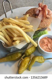 Lunch In A Cafe. French Fries In A Metal Basket, Marinated Green Chili Pepper, Cheeseburger And A Sauce. Hamburger With Beef, Lettuce, Ham, Cheese, Cucumber And A Delicious Bun With Sesame. Fast Food 