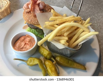 Lunch In A Cafe. French Fries In A Metal Basket, Marinated Green Chili Pepper, Cheeseburger And A Sauce. Hamburger With Beef, Lettuce, Ham, Cheese, Cucumber And A Delicious Bun With Sesame. Fast Food 