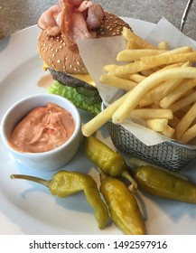 Lunch In A Cafe. French Fries In A Metal Basket, Marinated Green Chili Pepper, Cheeseburger And A Sauce. Hamburger With Beef, Lettuce, Ham, Cheese, Cucumber And A Delicious Bun With Sesame. Fast Food 