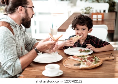 Lunch in cafeteria. Happy bearded father and cute funny son having lunch in cafeteria eating yummy pizza