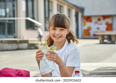 Lunch At School. A Charming Girl Is Eating Breakfast, A Snack At Recess In The Schoolyard. Nutrition For Children From Educational Institutions