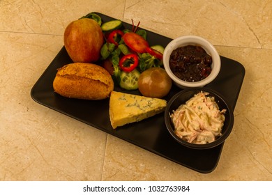 Ploughmanâ??s Lunch With Stilton Cheese, Pickle, Pickled Onion, Salad, Coleslaw And Bread Roll And Apple.