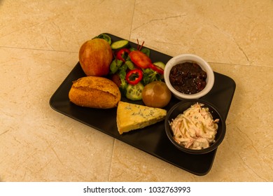 Ploughmanâ??s Lunch With Stilton Cheese, Pickle, Pickled Onion, Salad, Coleslaw And Bread Roll And Apple.