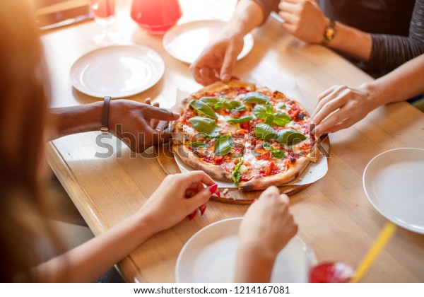 Lunch\
time at pizzeria, multiracial people grabbing huts of delicious\
pepperoni pizza, close up. Food and Party\
concept