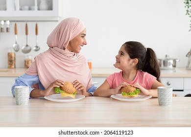 Lunch Together. Cute Little Girl And Her Young Muslim Mom In Hijab Eating Sandwiches In Kitchen, Happy Islamic Lady And Adorable Female Child Enjoying Tasty Meal And Smiling To Each Other, Copy Space