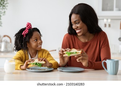 Lunch Together. Little Black Girl And Her Happy Mother Eating Sandwiches In Kitchen, Cheerful African American Mom And Cute Female Child Enjoying Tasty Meal And Smiling To Each Other, Copy Space