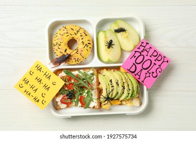 Lunchbox With Fake Spider, Bugs And Happy Fools' Day Note On White Wooden Table, Top View