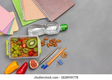 Lunchbox With Nuts And Fruits. Pens And Notebooks, Note Paper. Bottle Of Water. Grey Background. Flat Lay
