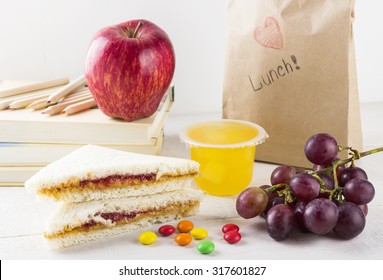 Lunchbox In School: Sandwich With Peanut Butter And Jam, Apple, Grapes, Jelly On A White Wooden Background