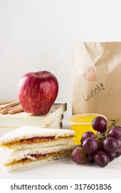 Lunchbox In School: Sandwich With Peanut Butter And Jam, Apple, Grapes, Jelly On A White Wooden Background