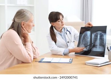 Lung disease. Doctor showing chest x-ray to her patient at table in clinic - Powered by Shutterstock