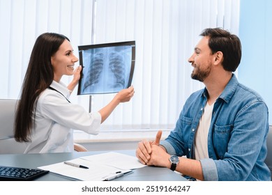 Lung disease. Young female doctor showing chest x-ray to her male patient man at table in modern clinic explaining diagnosis, discussing scan results in hospital office while appointment. - Powered by Shutterstock