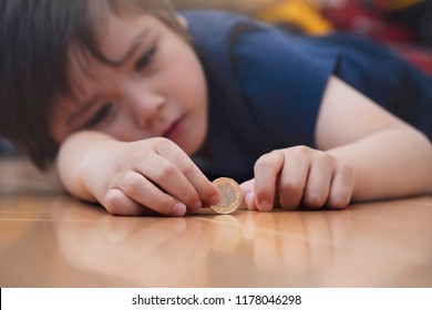 lurry image of Kid with thinking face laying dow on wooden floor holding one pound money coin, Selective focus of Unhappy child playing with new British one pound coin,Spoiled kid