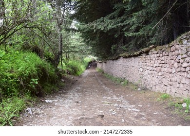 Luscious peaceful dirt stone path with timber picket fence and rock wall among green grass. Cusco, Peru