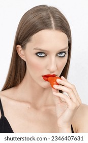 Luscious red lips. Portrait of a beautiful young woman biting into a strawberry.