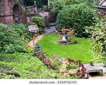 A lush backyard garden with vibrant greenery, colorful flowers, a stone path, and a birdhouse, featuring a person bent over tending to the plants. - Powered by Shutterstock