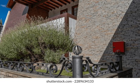 Lush blooming lavender grows against the wall of the house. There is an openwork metal fence around the lawn. El Calafate. Argentina - Powered by Shutterstock