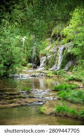 Lush forest stream winding through mossy rocks and small cascading waterfalls, surrounded by dense green foliage. A peaceful, natural landscape conveying serenity, freshness and untouched outdoor beauty. in Baume-les-Messieurs france