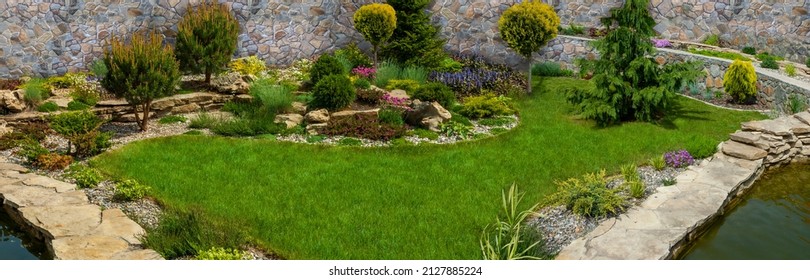 Lush Green Botanical Garden - Blooming Spring Flowers And Lawn Path,with Grass Growing Up Between The Stones.Beautiful Small Garden Pond With Stone Banks And Ornamental Plants.