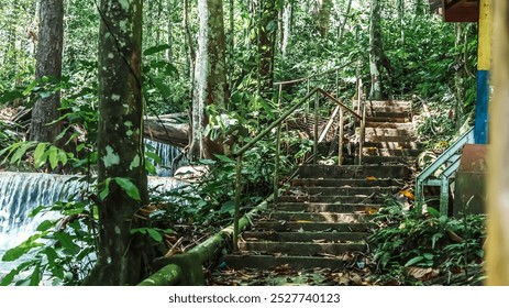 A lush green forest with a waterfall and a staircase leading up to a building. The waterfall is a beautiful and calming sight, with the water cascading down the rocks and creating a soothing sound - Powered by Shutterstock