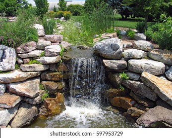 A lush green garden with waterfall cascading down the rocky stones - Shutterstock ID 597953729