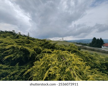 Lush greenery covers the foreground leading to distant ancient stone formations set against a backdrop of dark, dramatic clouds. The landscape evokes a sense of history. - Powered by Shutterstock