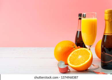 Lush Mix Drink, Summer Alcoholic Beverages And Refreshing Mimosa Cocktail Concept With Oranges, Champagne Flute And Bottles Of Bubbly Isolated On White Wooden Table And Pink Background With Copy Space