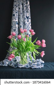 Lush natural light old Dutch Delft blue pink tulips in a glass vase on navy blue linen against a black background.