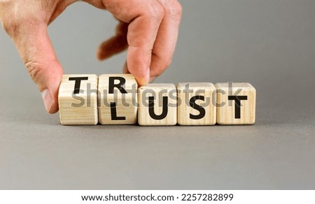 Lust or trust symbol. Businessman turns wooden cubes and changes the words 'lust' to 'trust'. Beautiful grey table, grey background. Business and lust or trust concept, copy space.